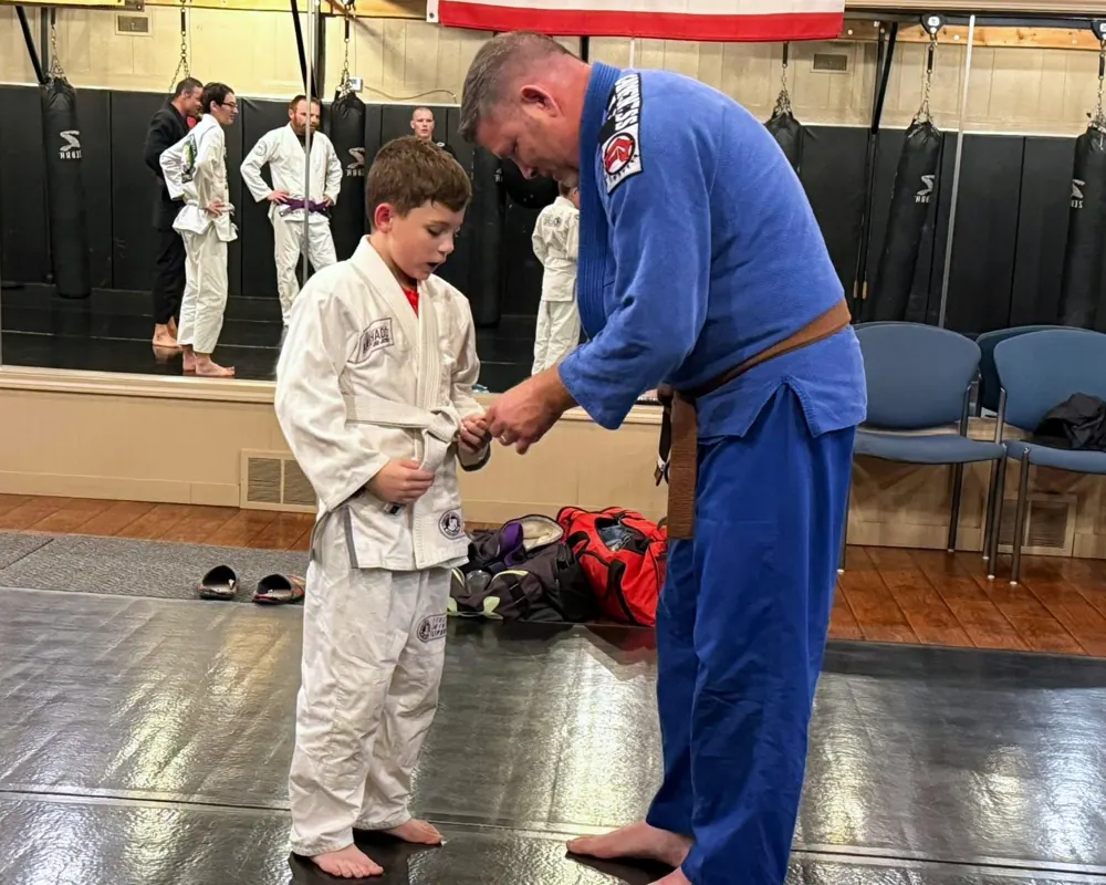 An instructor ties a young student's white belt before class.