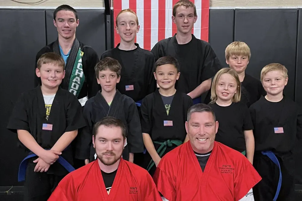 Students in black uniforms stand with two instructors in red after a belt test.