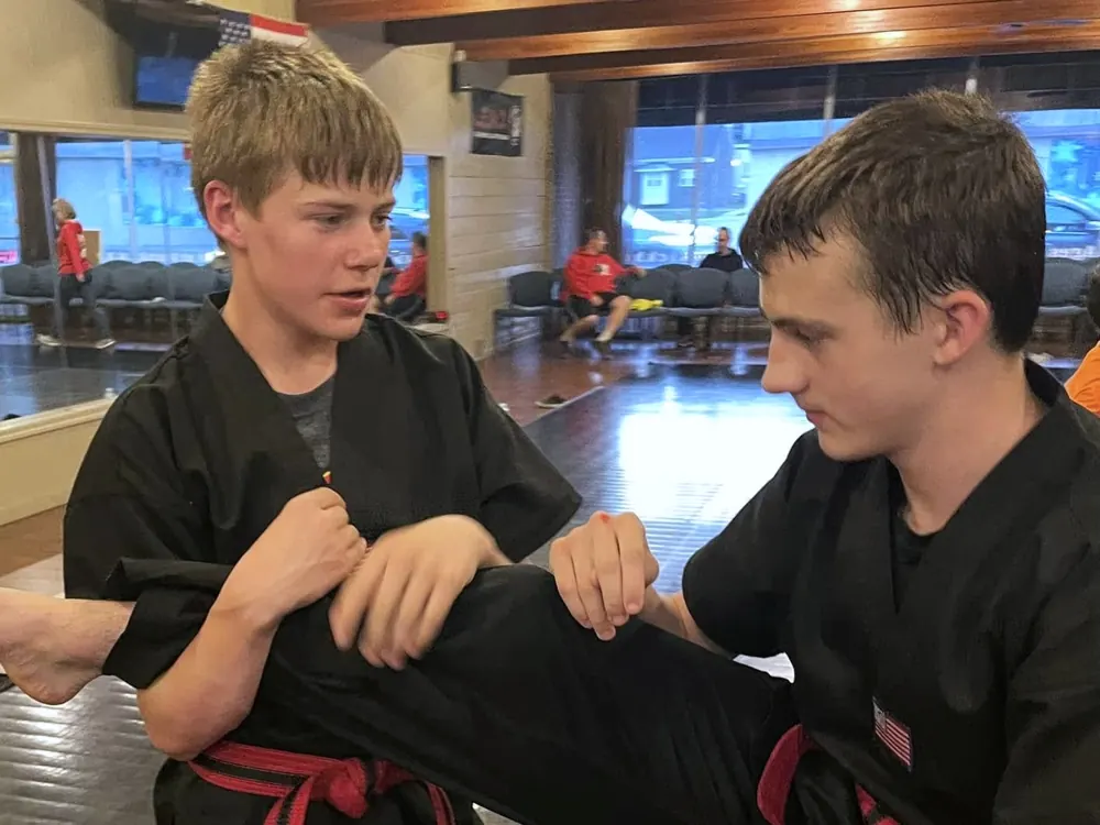 Two students in black uniforms practice a hold together on the mat.